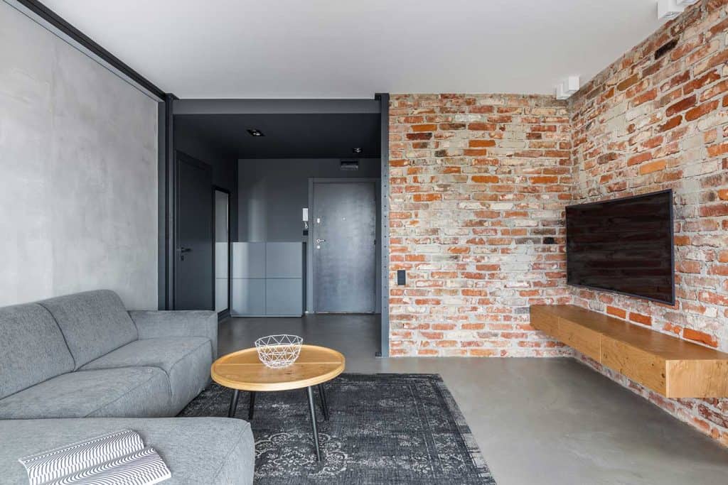 Mur en briques apparentes et sol en béton dans un salon industriel avec canapé et tapis gris