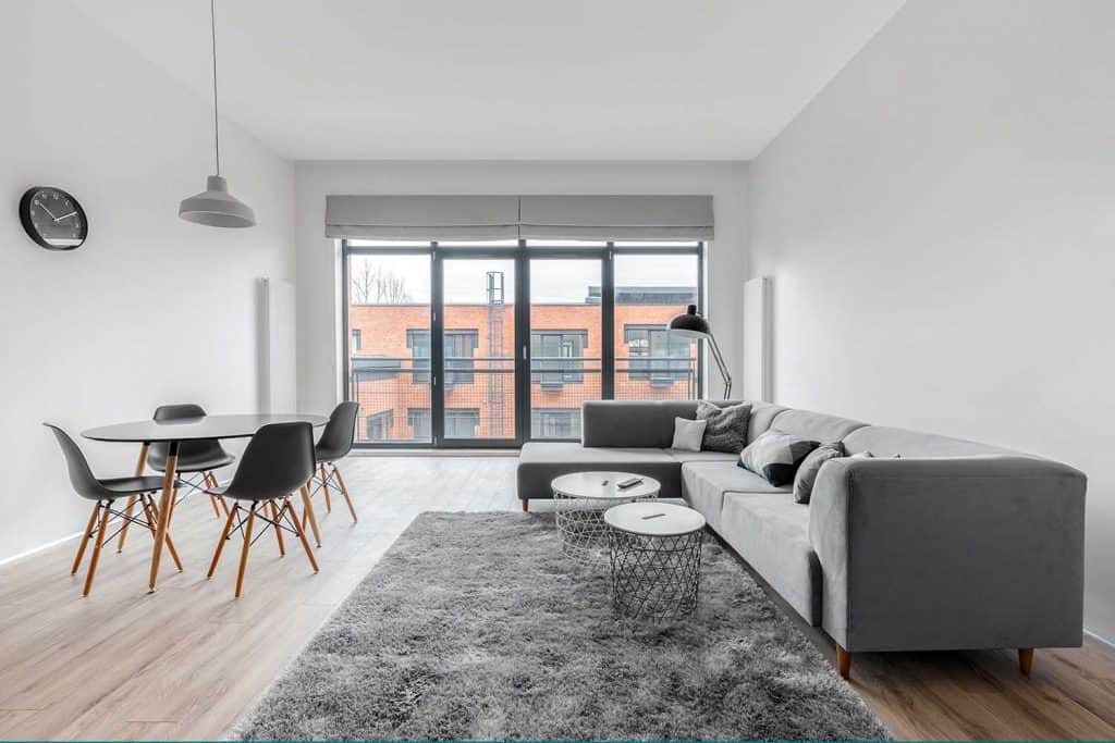 Modern and stylish living room with window wall, dining area, gray corner sofa and rug