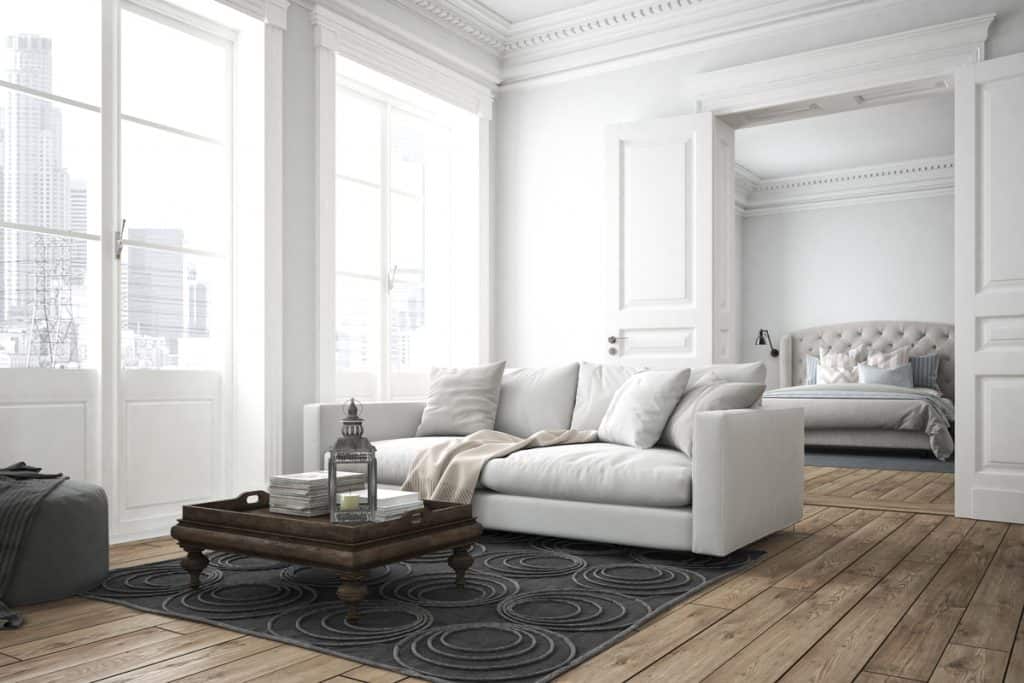 Een woonkamer met wit geschilderde muren, wit gekleurd kroonlijst gecombineerd met witte banken en houten vloeren