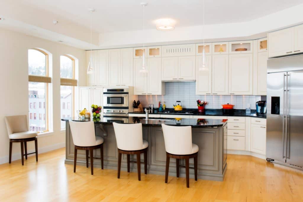 A modern dining room with hardwood floors, white dining chairs, white paneled cabinets, and a black granite countertop