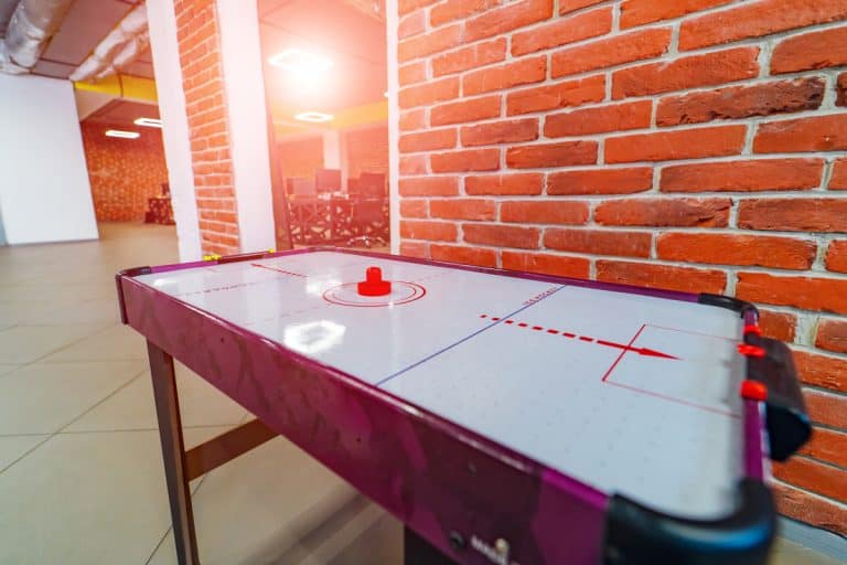 An air hockey table at an entertainment area of a house with brick walls, How Much Does a Good Air Hockey Table Cost