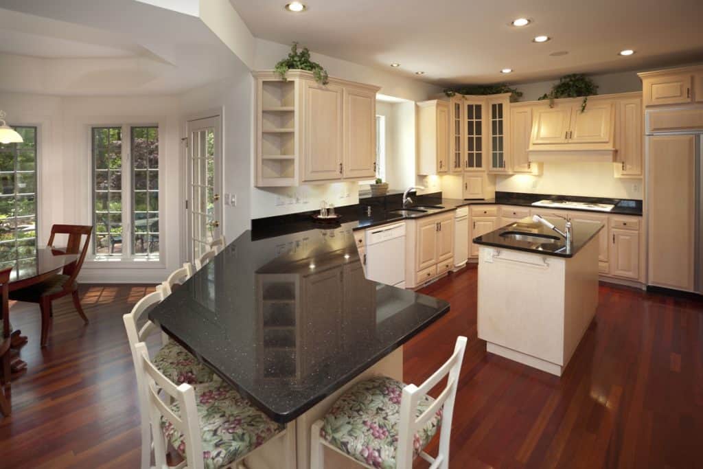 A classic modern kitchen with wooden vinyl flooring, black granite countertops, and white colored cabinet panels