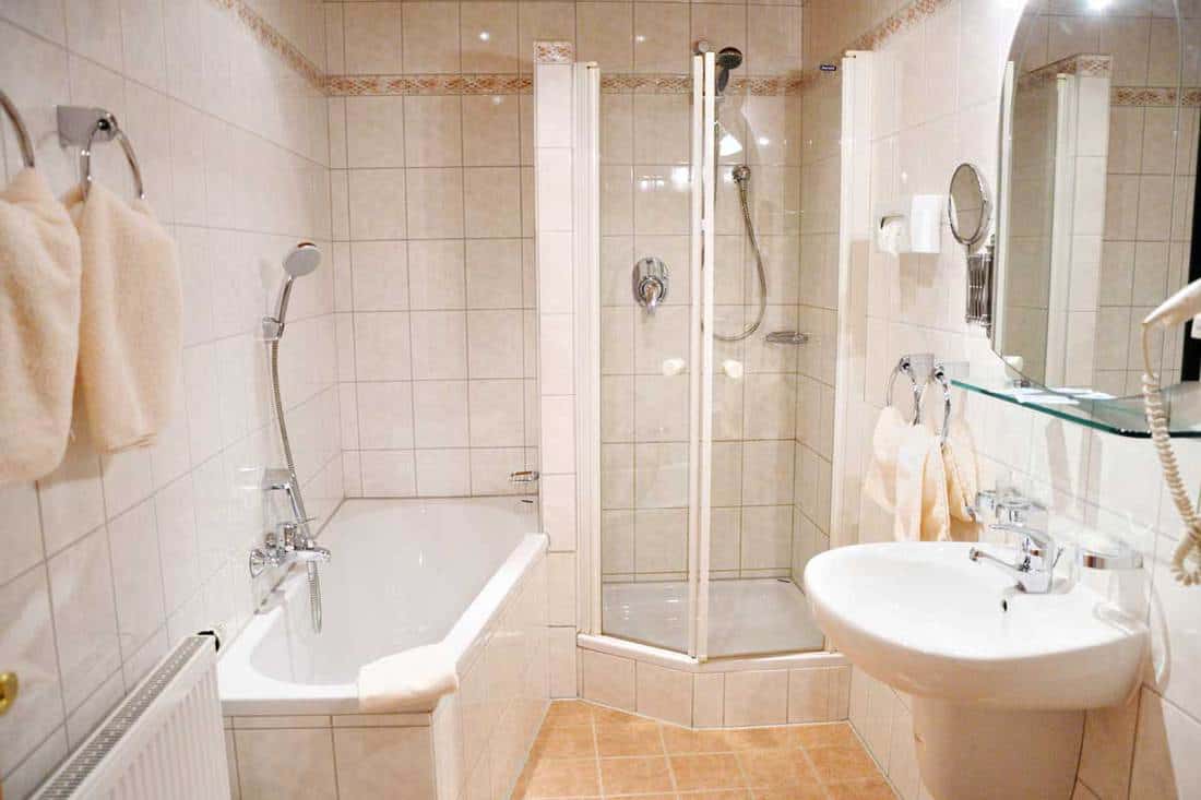 Beautiful spacious light bathroom with Bright tiles, white bath, shower, sink, large and cosmetic mirror, towels
