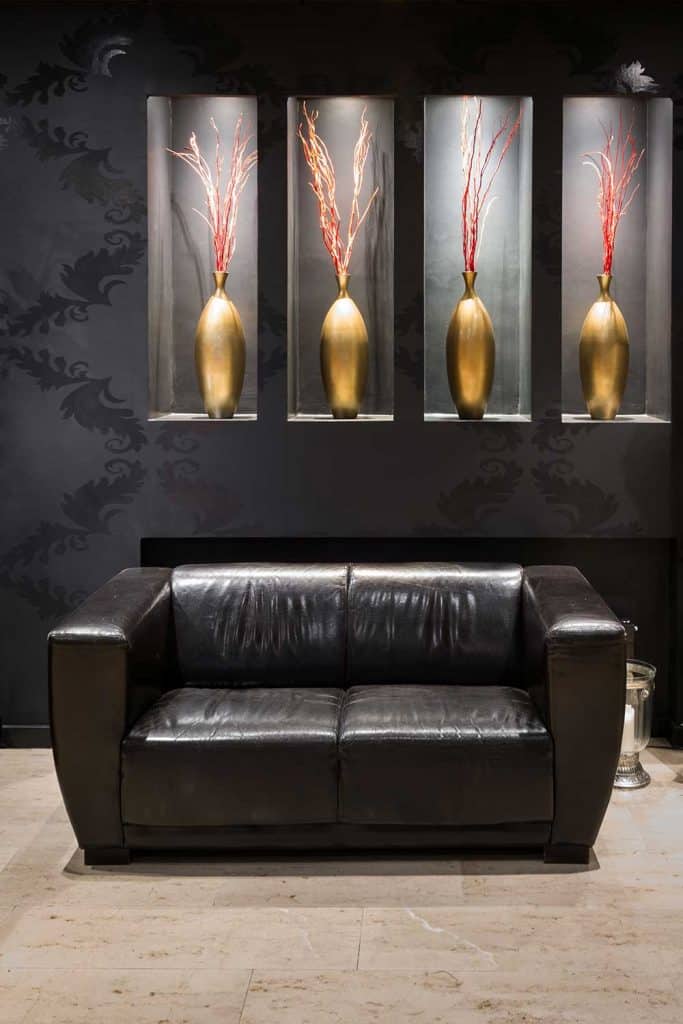 Black leather couch in anteroom with golden flower vase