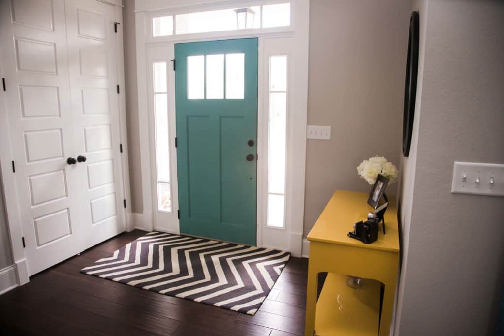 Black patterned rug in an entryway with a turquiose color front door and hardwood flooring