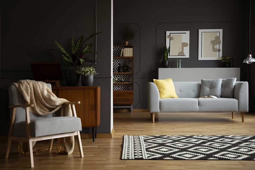 Couverture sur fauteuil à côté d'un tapis à motifs à l'intérieur du salon avec canapé gris