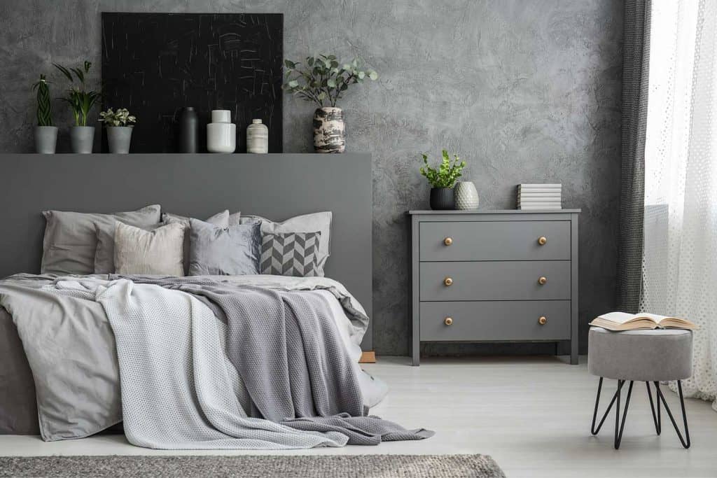 Intérieur de chambre gris monochromatique avec un grand lit avec des coussins et une armoire à tiroirs contre un mur avec une toile noire