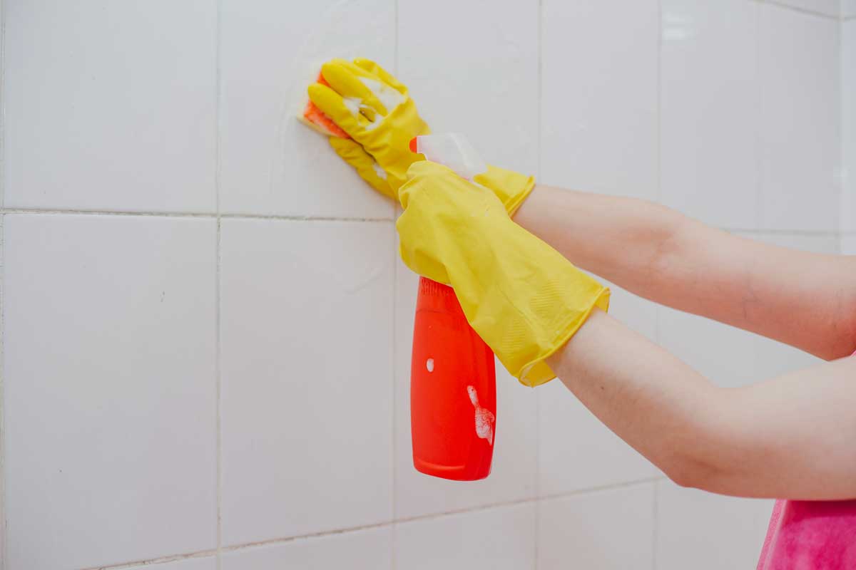 Woman in rubber gloves cleaning the bathroom shower tiles