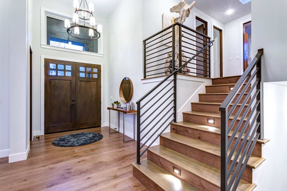 A beautiful foyer with white painted walls, wooden flooring and a modern design stairs