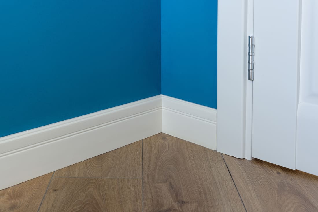 A blue walled room with a white colored baseboard and a wooden floor, What Is The Best Paint For Baseboards? [4 Actionable Suggestions]