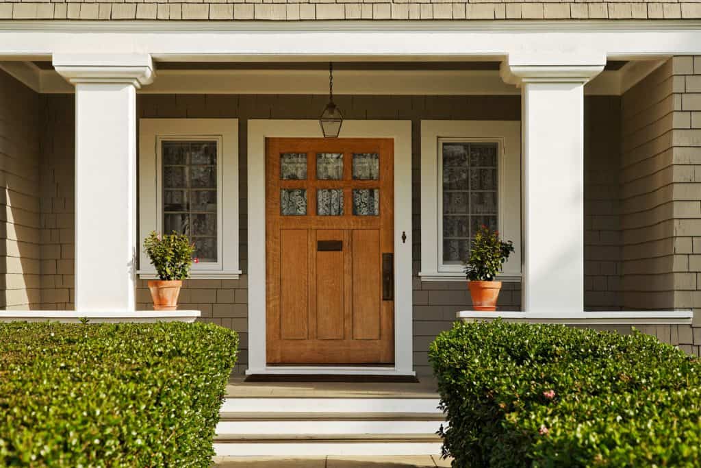 A concrete walkway bordered with hedged shrubs leads to the front door of a home
