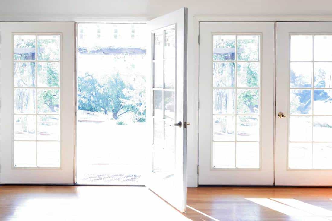 A door is open in a brightly lit room full of French doors and hardwood flooring