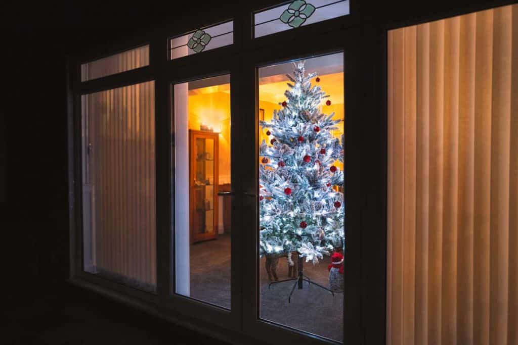 A frosted white artificial christmas tree with red and silver decorations seen through large french doors with vertical slat blinds , Can You Put Blinds On French Doors? (And How To)