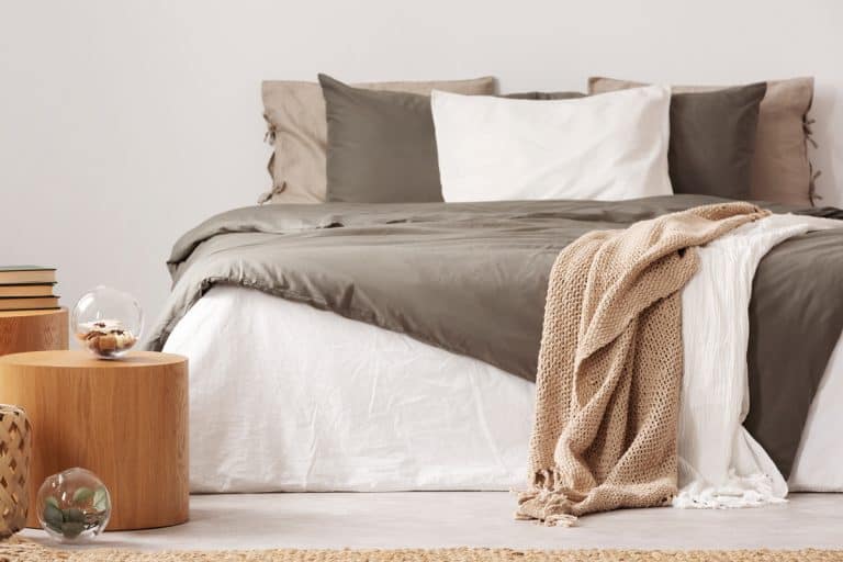 A gorgeous bed with pillows, brown blanket and a small round wooden nightstand, 5 Warmest Blankets For Your Bed [By Material]