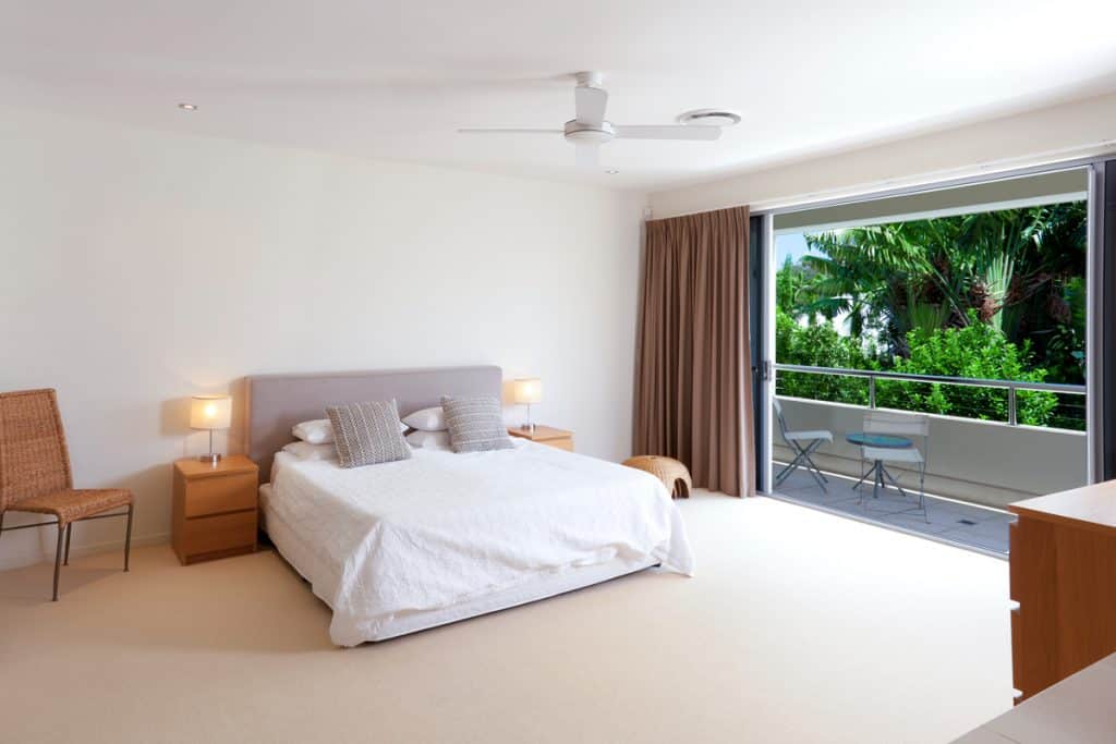 A large bedroom with white beddings and gray pillows, brown curtains on the huge window