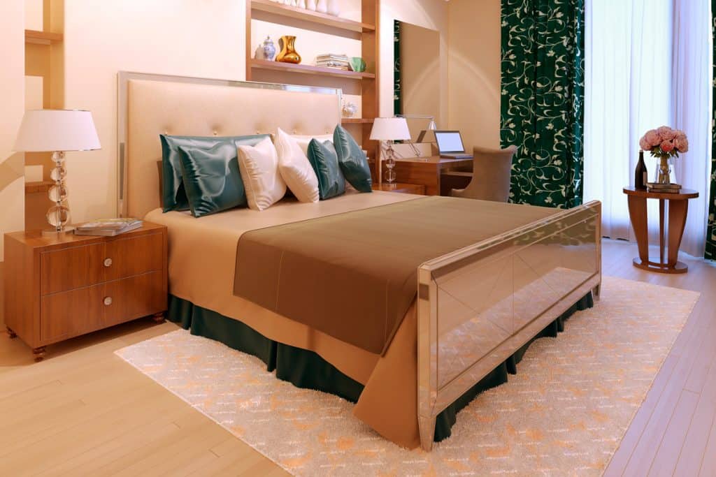 A luxurious bedroom with a beige colored headboard dark green floral curtains and an area rug under the bed