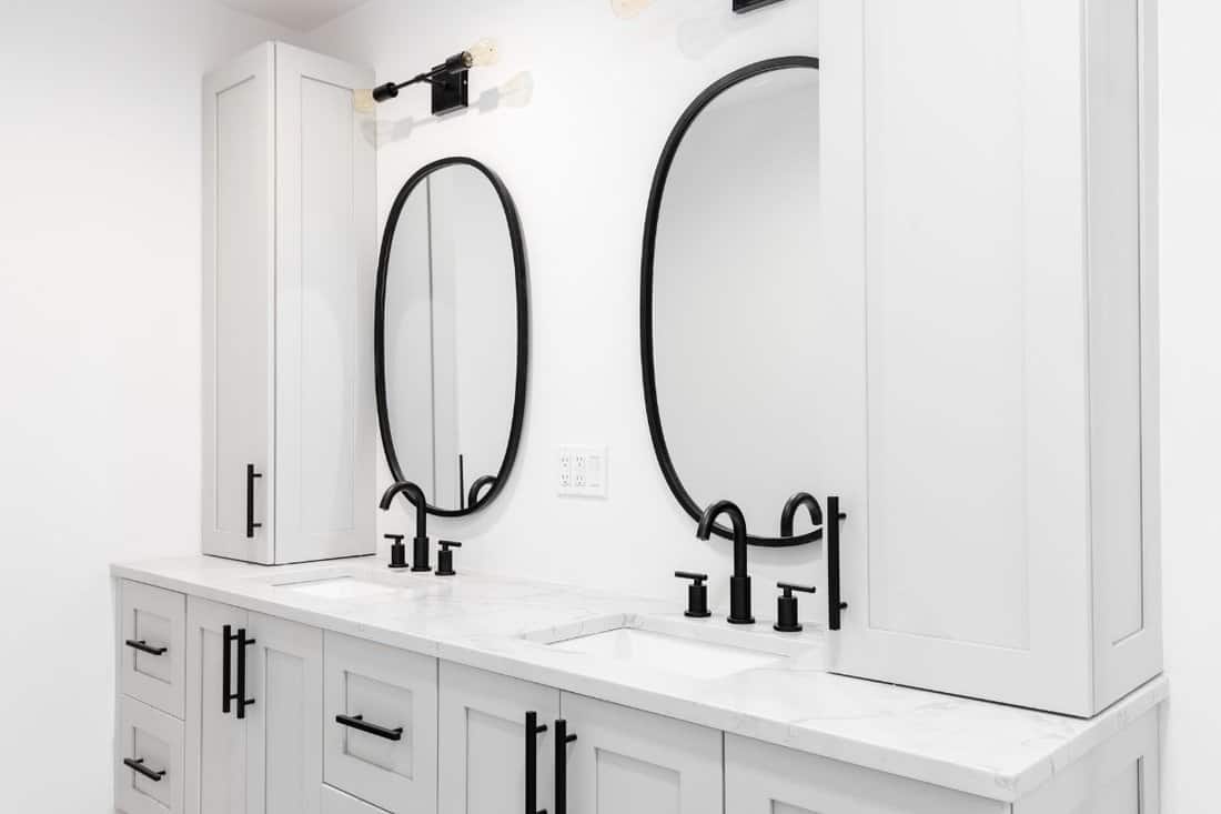 A luxury bathroom with a grey double vanity cabinet, black faucets and lights, and a white marble countertop.