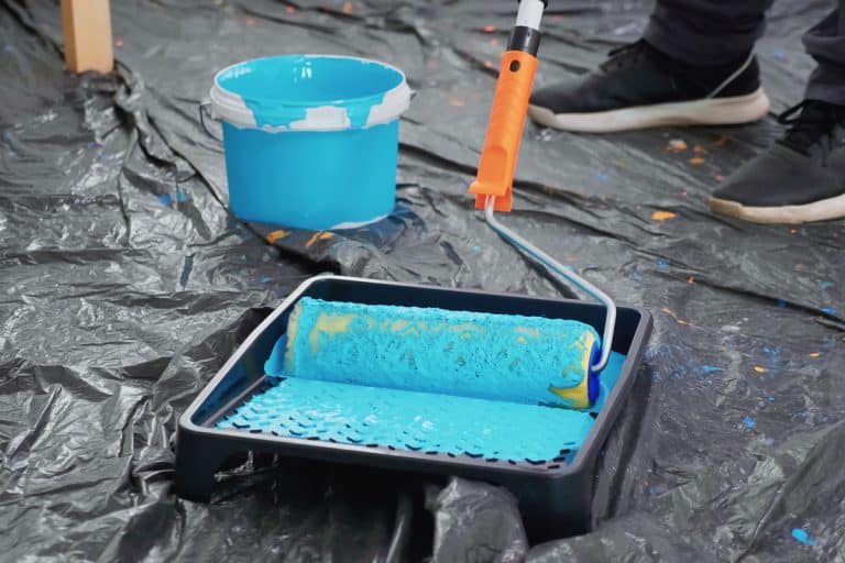 Man rolling his rolling pin on the paint tray with blue paint mixed with latex, How To Thin Latex Paint [5 SIMPLE Steps]