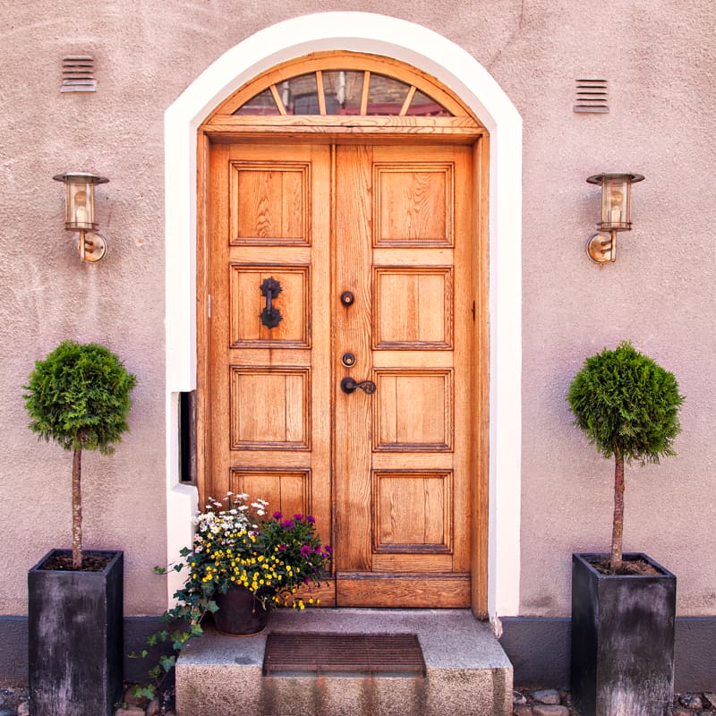A Mediterranean style hardwood front door with side plants on the porch