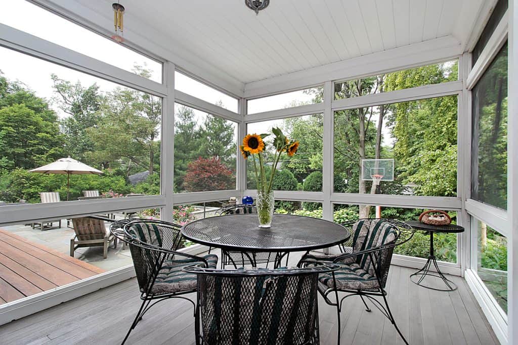Un porche d'inspiration moderne avec des chaises et une table en acier et un vase avec un tournesol sur le dessus de la table