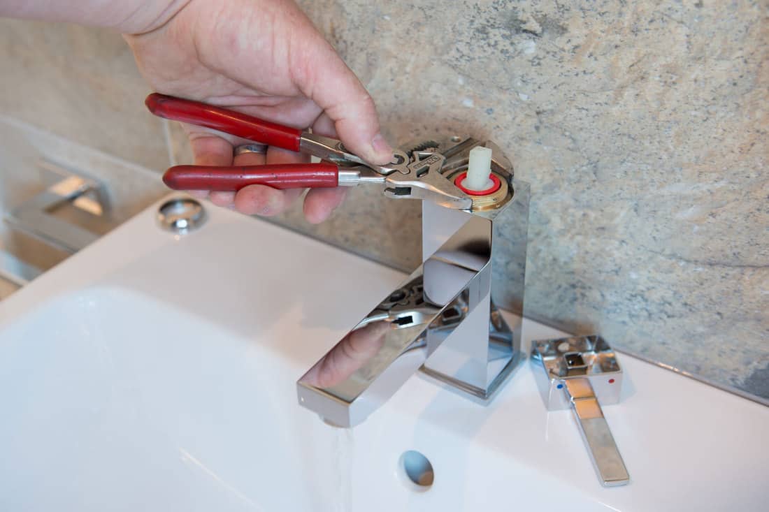 A plumber uses adjustable grips to carry out a repair on a faucet/tap for his client's new bathroom sink, How Long Does It Take To Install A New Bathroom Sink?