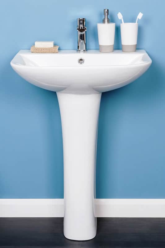 A vertical shot of a white modern pedestal bathroom sink with soap and toothbrushes