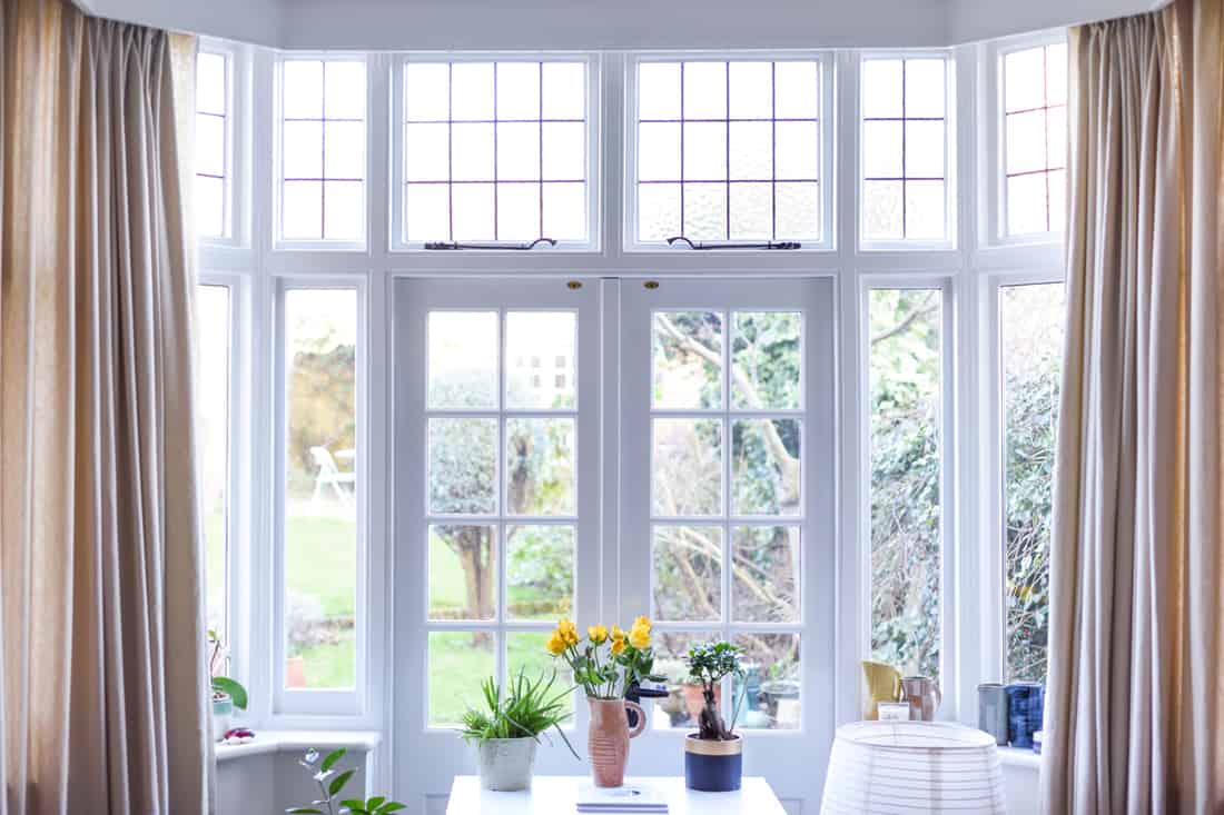 A white themed dining room with white painted walls and a wooden framed bay window with a French Door, How To Fix Misaligned French Doors? 