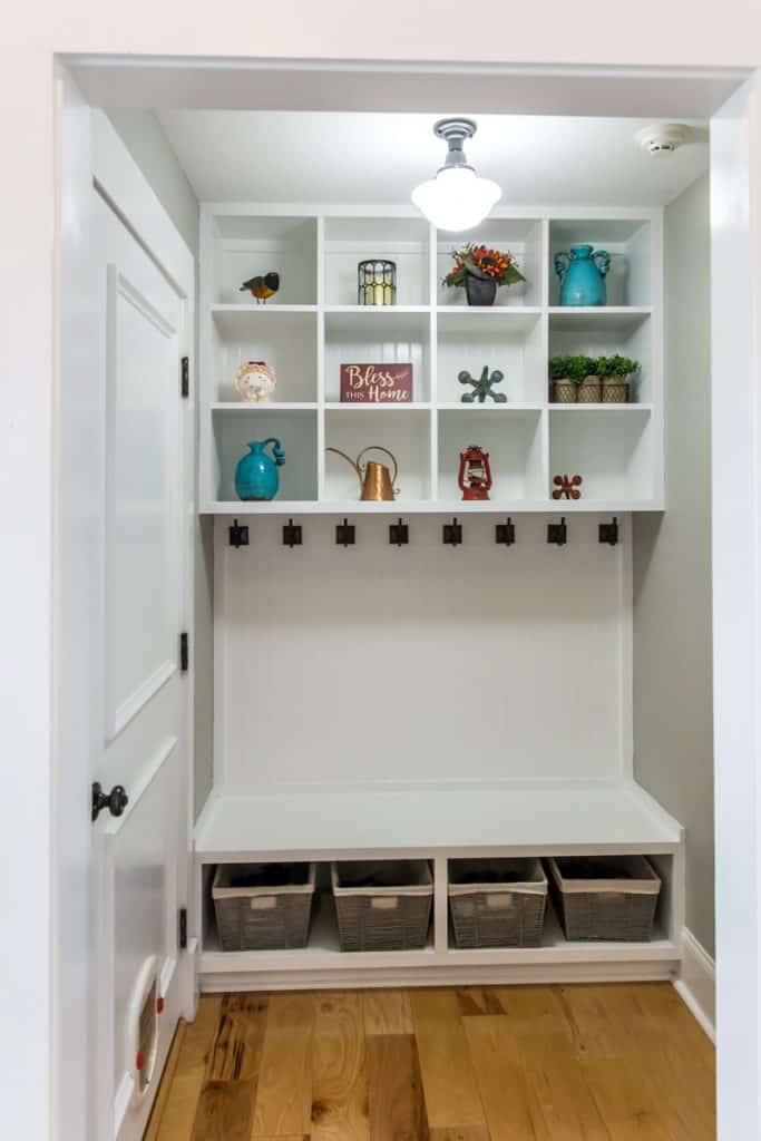 An entryway with overhead cabinets and a coat rack right underneath the cabinets with an extra shoe section on the bottom