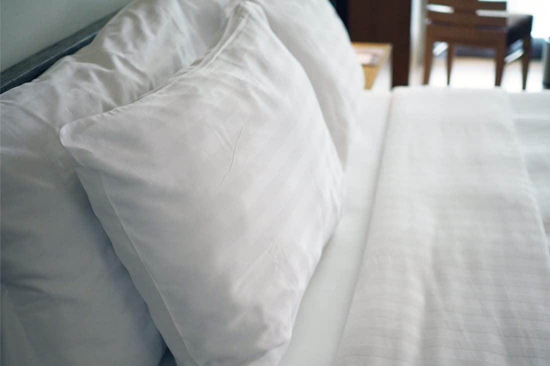 Big white soft pillows on a white luxury cozy bed with clean white sheets, how to wash feather pillows