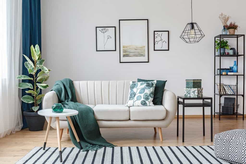 Table noire à côté d'un canapé avec couverture verte dans un appartement confortable avec galerie d'affiches