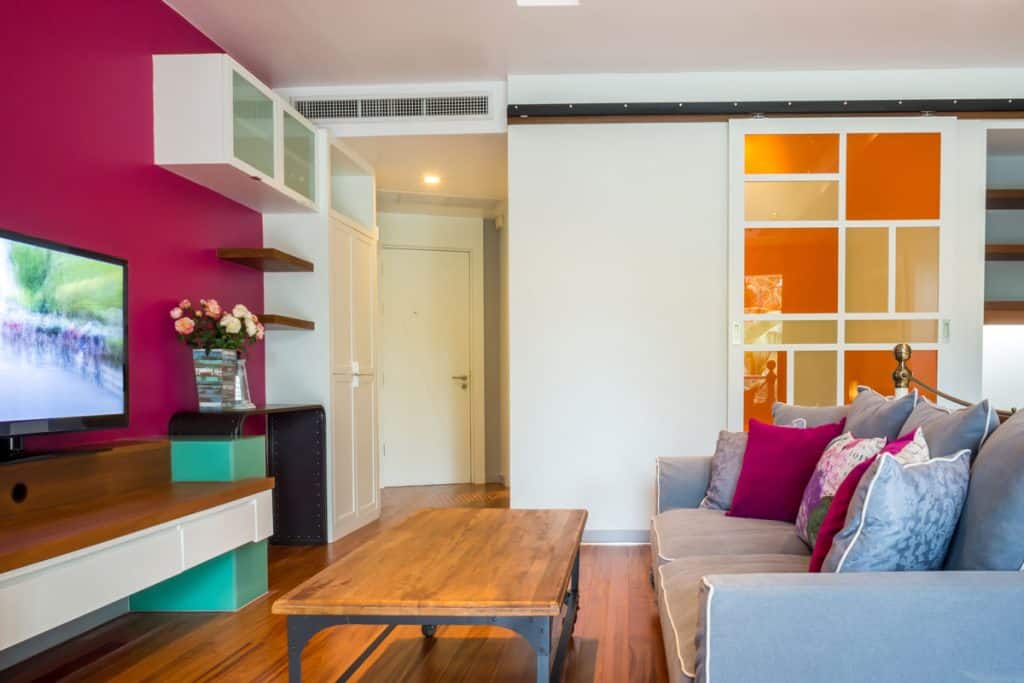 Bright colored living room with a magenta accent wall and white wall with wooden flooring