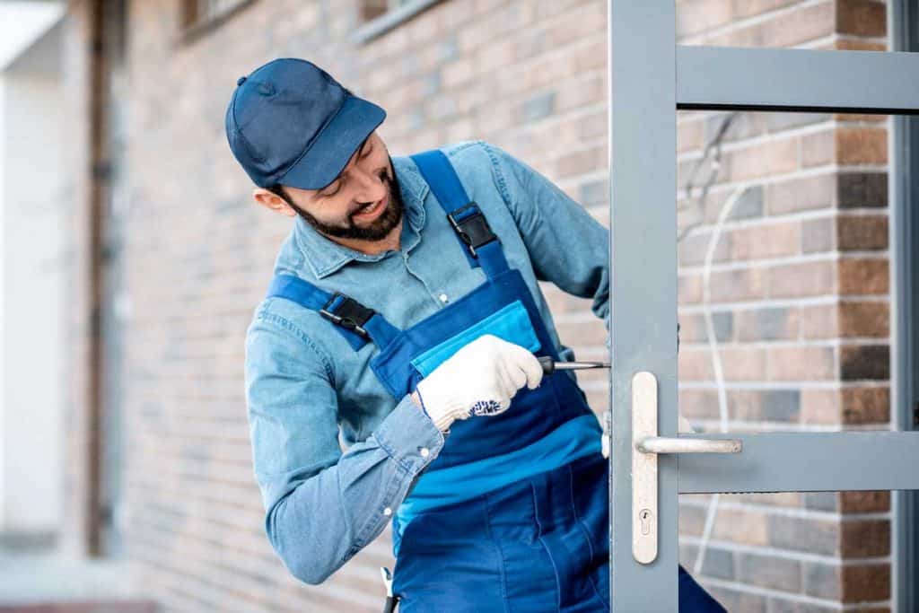 Builder in uniform installing a door lock into the entrance door of a new house