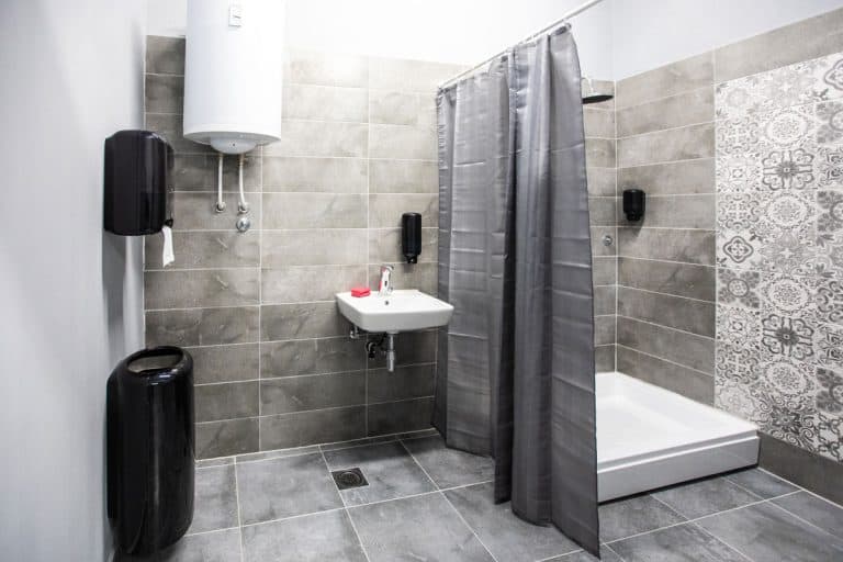 A gray themed bathroom with gray tiles on the floor and wall matched with a gray shower curtain, How Long Is A Shower Curtain? [Standard Shower Curtains Sizes]
