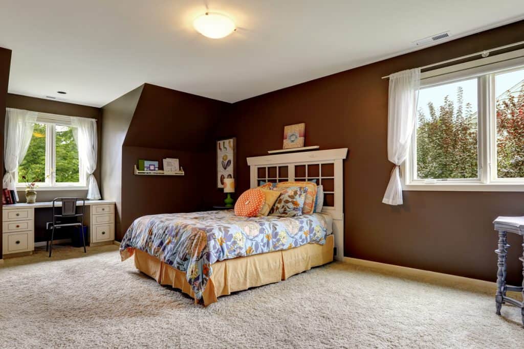 Grande chambre avec murs peints en marron, literie florale et rideaux blancs à la fenêtre