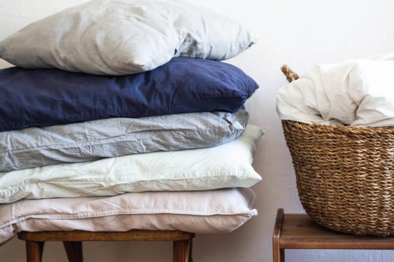 Large pillows of various colors on a chair and a large wicker basket with a white blanket, How Often Should You Change Your Pillowcase?