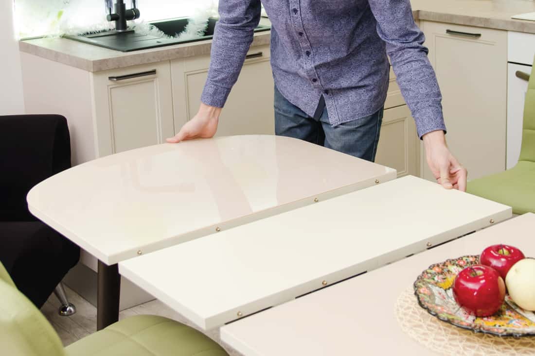 Man lays out a sliding glossy dining table on which stands a plate with artificial fruit.