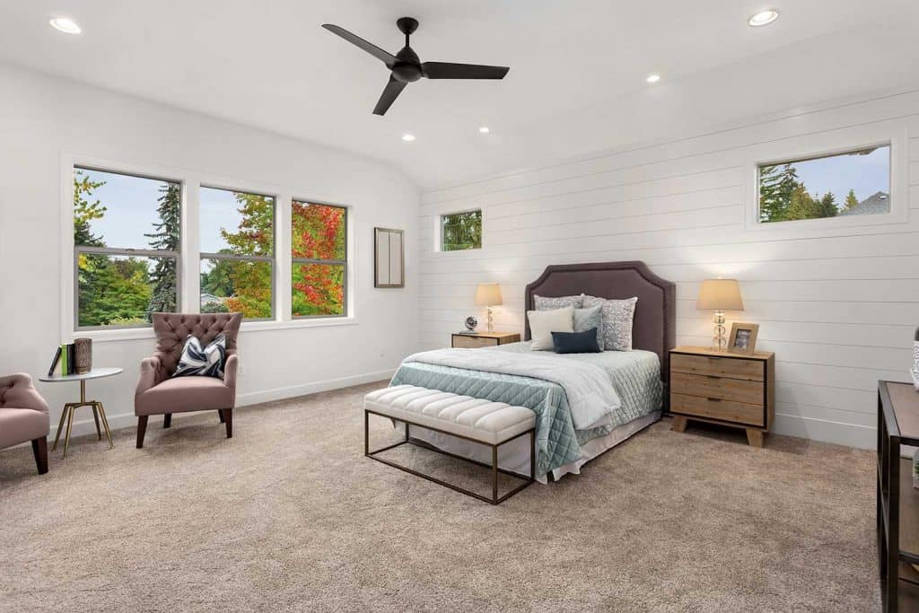 Master bedroom in new luxury home with large windows, ceiling fan, carpet, and elegant decor