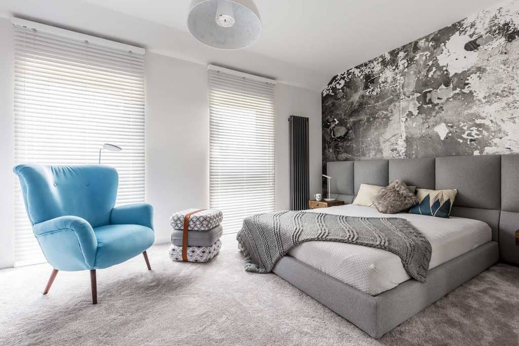 Chambre grise monochromatique avec mur grunge, table de chevet en bois, murs blancs et fauteuil de style vintage bleu