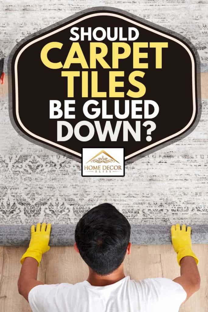 Male worker in overalls rolling carpet on floor at home, Should Carpet Tiles Be Glued Down?