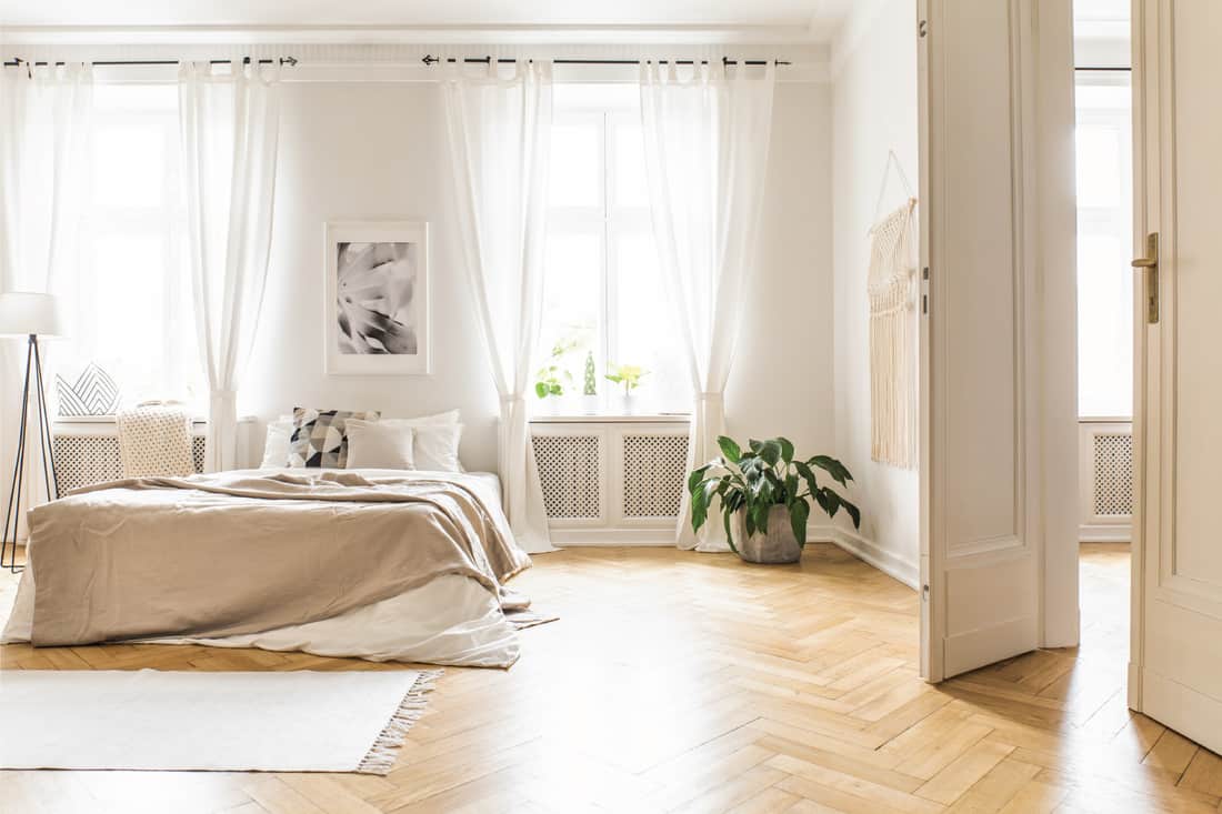 Spacious and bright bedroom interior with beige decorations, hardwood floor and a book on the window sill