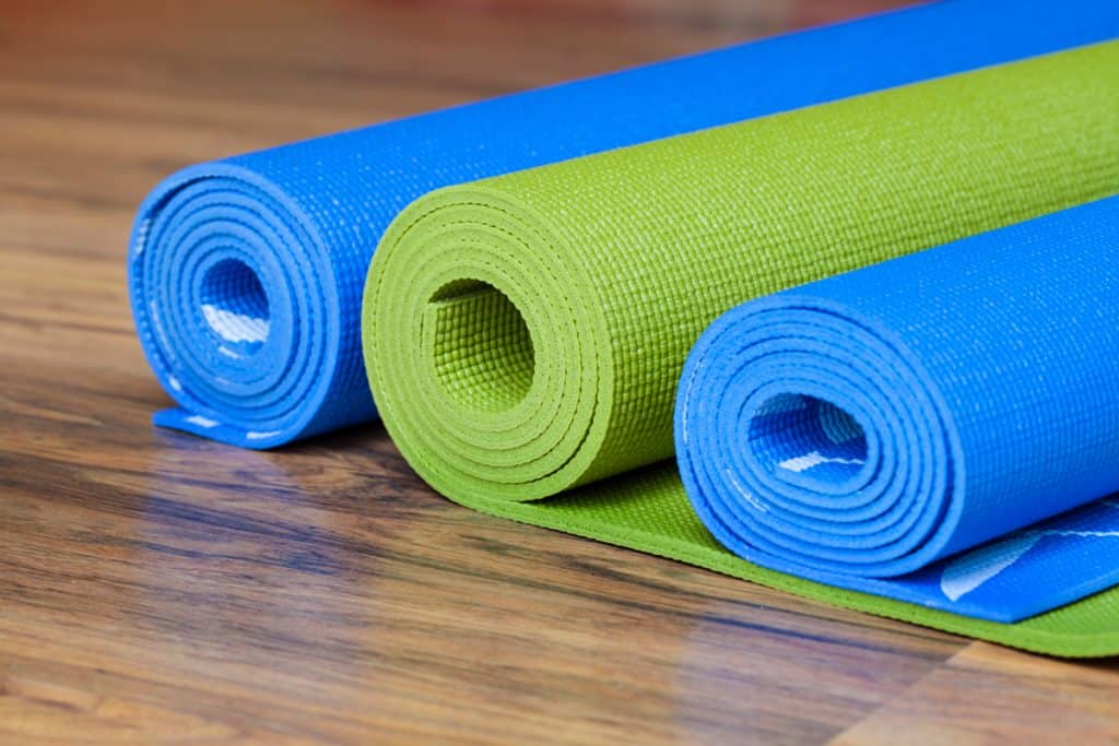 Three different colored yoga mats placed on a wooden floor for soundproofing