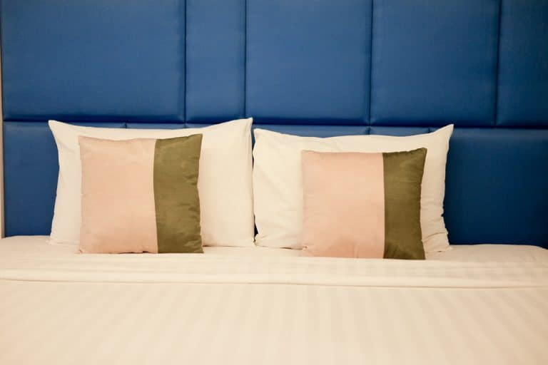White down pillows standing next to a blue wall with throw pillows placed next to it, How Long Do Down Pillows Last?