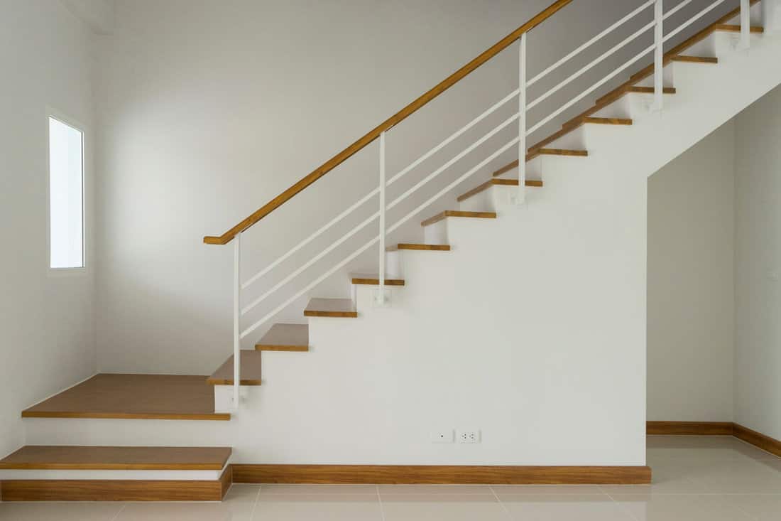 Wooden stairs with white walls and wooden stair handle and white metal railing