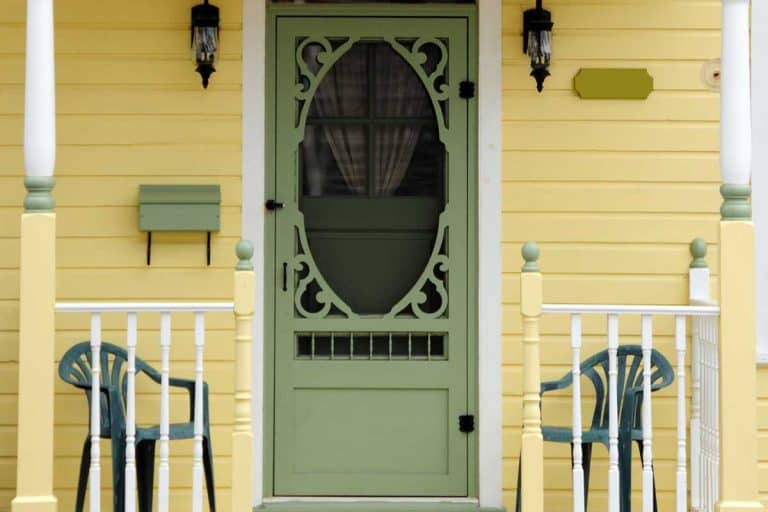 Yellow Victorian porch with green chairs and with an ornate green spring screen door, How Much Does A Screen Door Cost? [Price By type of door]