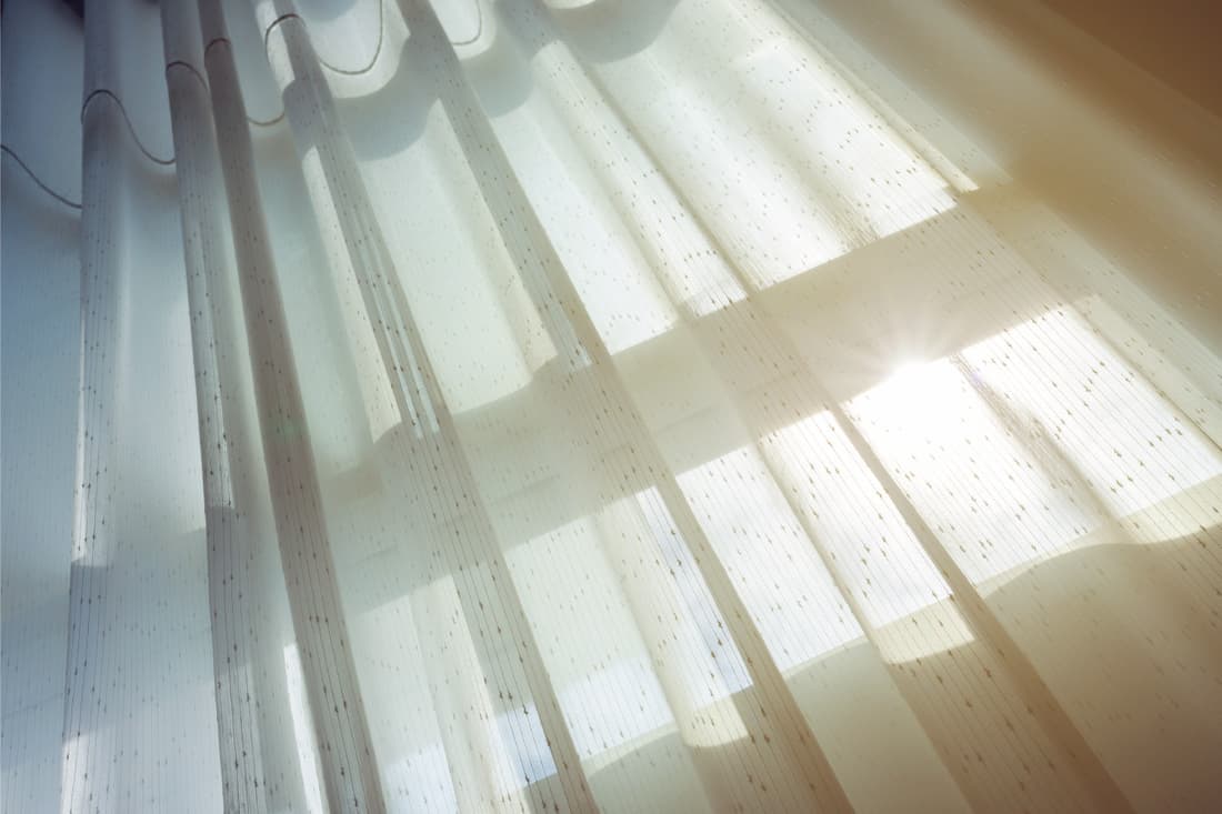Rideau en mousseline de voile aéré accroché à une fenêtre avec la lumière du soleil qui traverse
