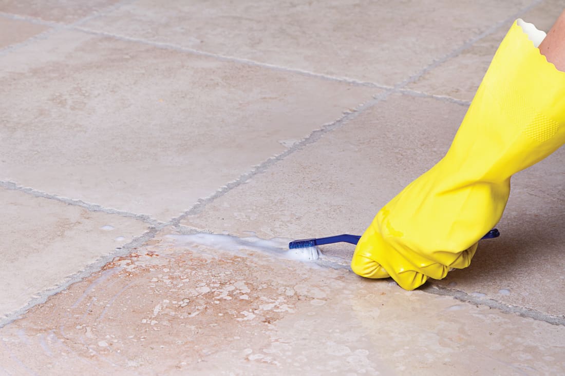 Hands with yellow rubber gloves cleaning tile grout with toothbrush