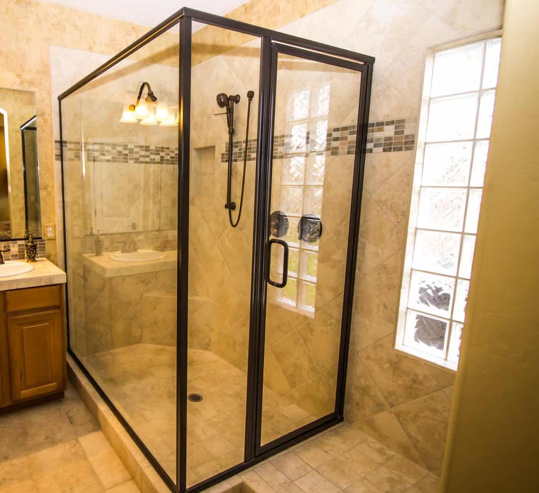 Douche en verre carrelée d'angle avec pulvérisateur à main dans une salle de bains moderne