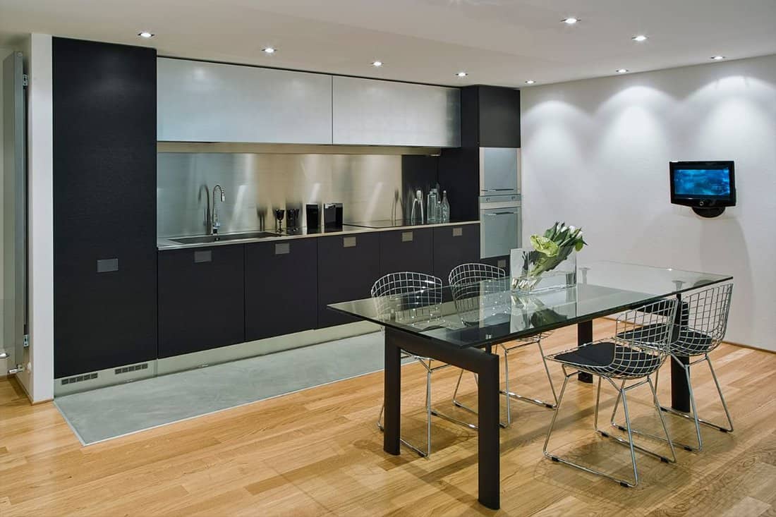 interiors shots of a modern kitchen in the foreground the glass dining table and iron chairs the floor is made of wood
