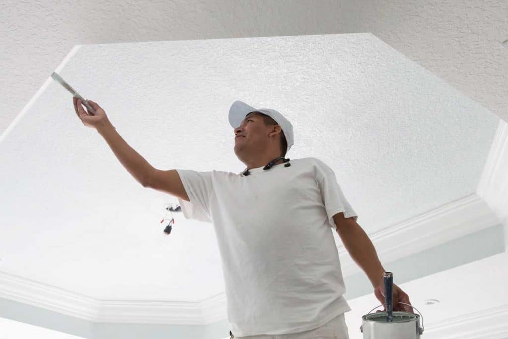 Painter painting the coffered ceiling in the bedroom of a home that is being redecorated