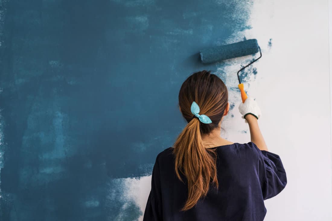 Girl holding a rolling pin paiting the wall with blue